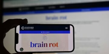 A man holds a phone, displaying word of ''brain rot''.